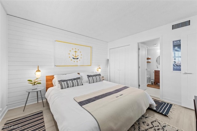 bedroom with a closet, light hardwood / wood-style floors, connected bathroom, and wooden walls