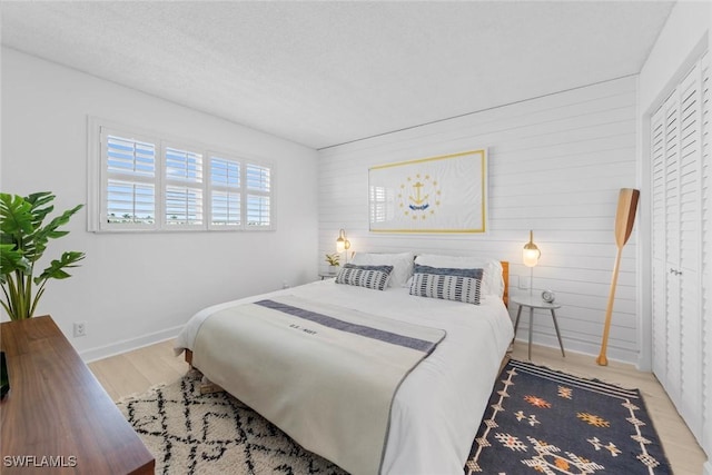 bedroom featuring a closet, wooden walls, a textured ceiling, and light hardwood / wood-style floors