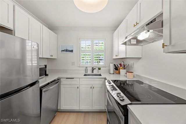 kitchen featuring white cabinets, appliances with stainless steel finishes, sink, ornamental molding, and light wood-type flooring