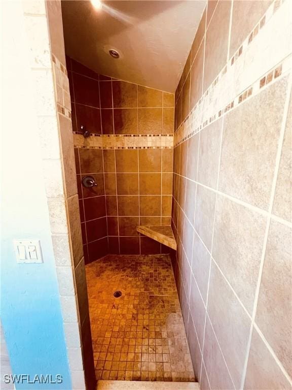 bathroom with lofted ceiling and tiled shower