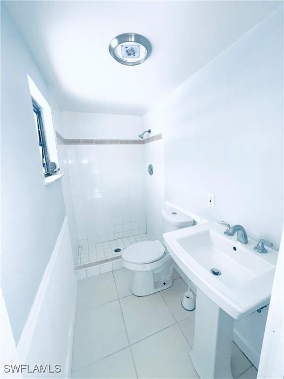 bathroom featuring tile patterned flooring, a tile shower, toilet, and sink