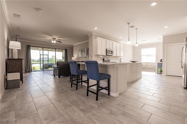 kitchen featuring a kitchen breakfast bar, hanging light fixtures, ceiling fan, appliances with stainless steel finishes, and white cabinetry