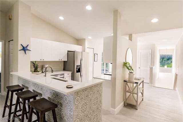 kitchen with white cabinets, a kitchen breakfast bar, sink, stainless steel fridge, and kitchen peninsula