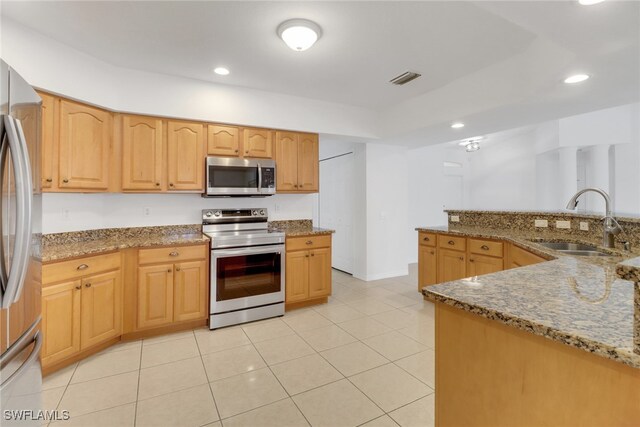 kitchen featuring light stone countertops, appliances with stainless steel finishes, light brown cabinetry, sink, and light tile patterned flooring