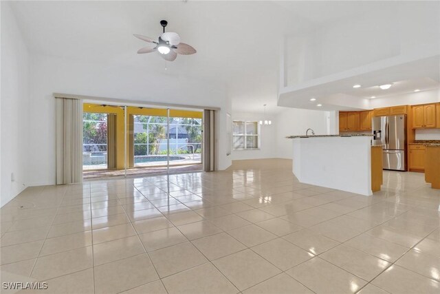 unfurnished living room featuring ceiling fan, light tile patterned floors, and a towering ceiling