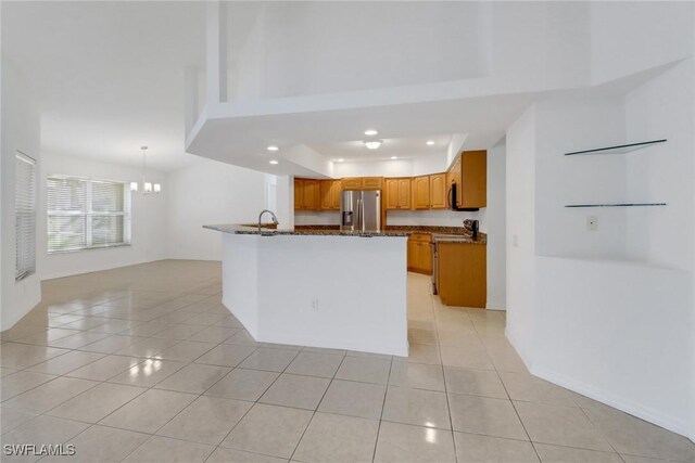 kitchen with appliances with stainless steel finishes, brown cabinets, dark stone countertops, and light tile patterned floors