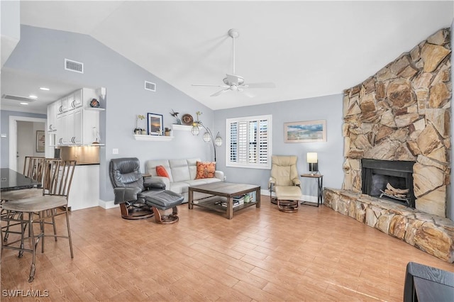 living room with lofted ceiling, ceiling fan, a stone fireplace, and light wood-type flooring