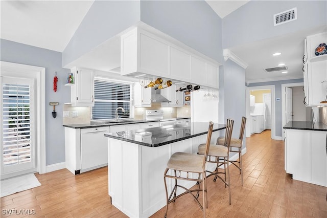 kitchen with white appliances, sink, wall chimney range hood, a center island, and white cabinetry