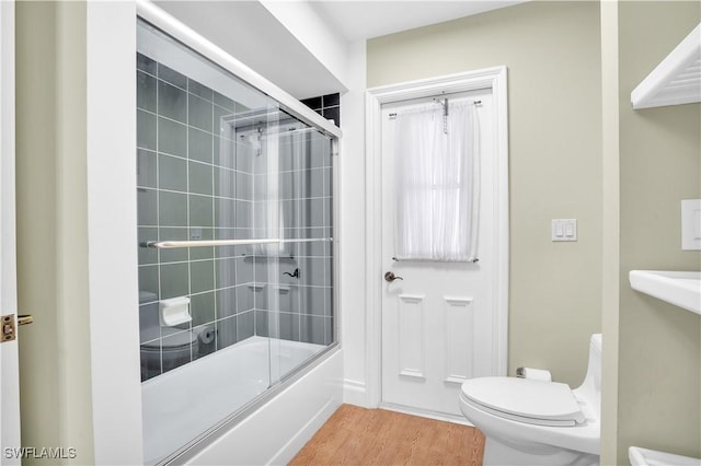 bathroom with hardwood / wood-style flooring, toilet, and shower / bath combination with glass door