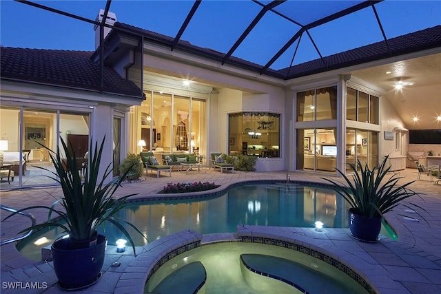 pool at dusk featuring glass enclosure, a patio area, and an in ground hot tub