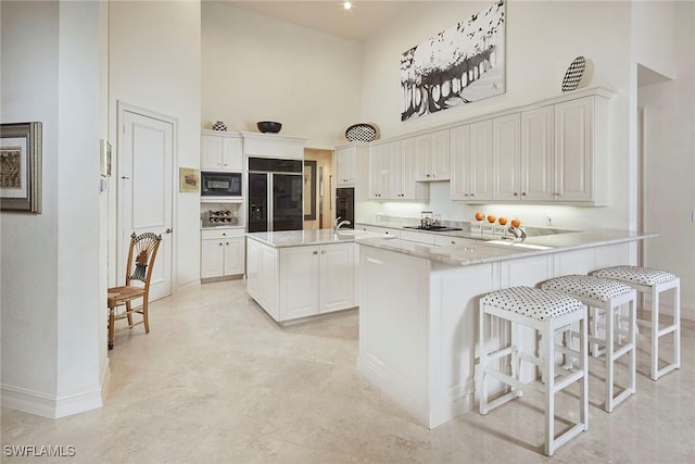 kitchen featuring kitchen peninsula, white cabinetry, a towering ceiling, and black appliances