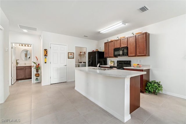 kitchen with light tile patterned flooring, sink, an island with sink, and black appliances