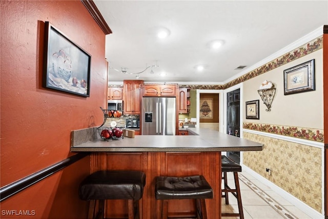 kitchen with a breakfast bar, light tile patterned floors, kitchen peninsula, stainless steel appliances, and crown molding