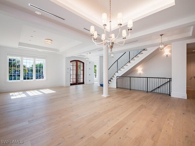 unfurnished living room with french doors, a tray ceiling, a chandelier, and light hardwood / wood-style flooring