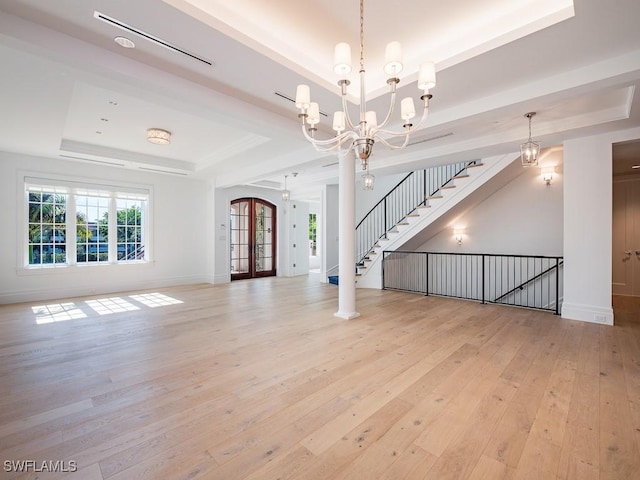 unfurnished living room featuring french doors, a notable chandelier, a tray ceiling, and light wood-type flooring