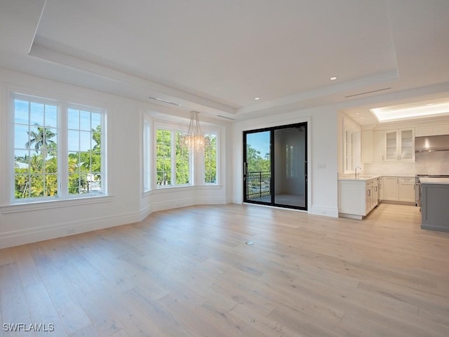 unfurnished living room with a raised ceiling, sink, and light hardwood / wood-style flooring