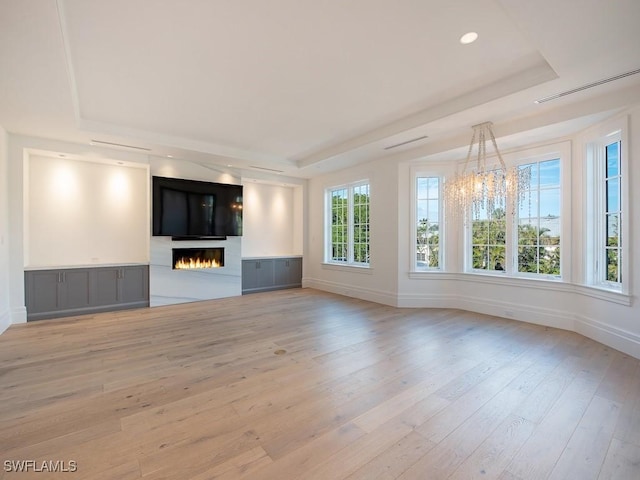 unfurnished living room with a notable chandelier, light hardwood / wood-style flooring, and a raised ceiling