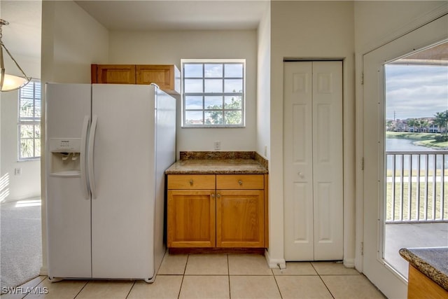 kitchen featuring white refrigerator with ice dispenser, light tile patterned floors, pendant lighting, and a water view