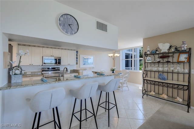 kitchen with kitchen peninsula, appliances with stainless steel finishes, light stone countertops, light tile patterned floors, and decorative light fixtures