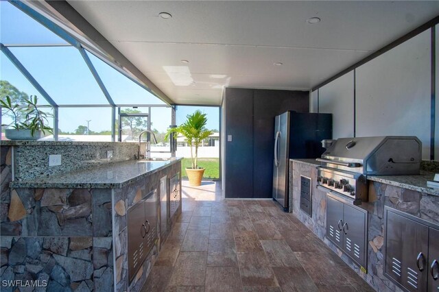 view of patio featuring a lanai, grilling area, sink, and an outdoor kitchen