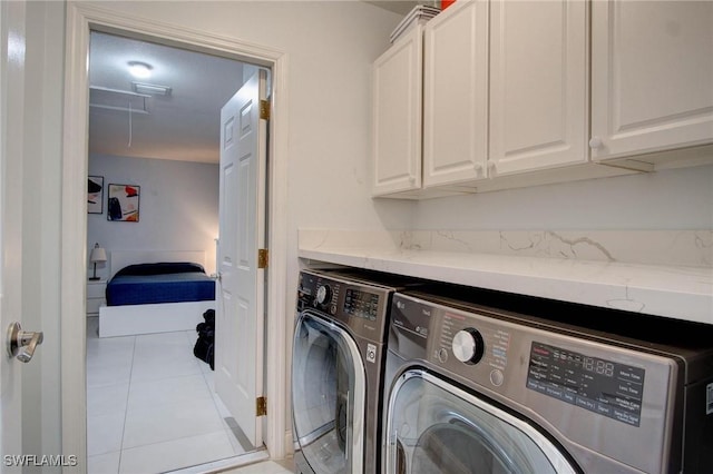 clothes washing area featuring cabinets, light tile patterned floors, and washing machine and dryer