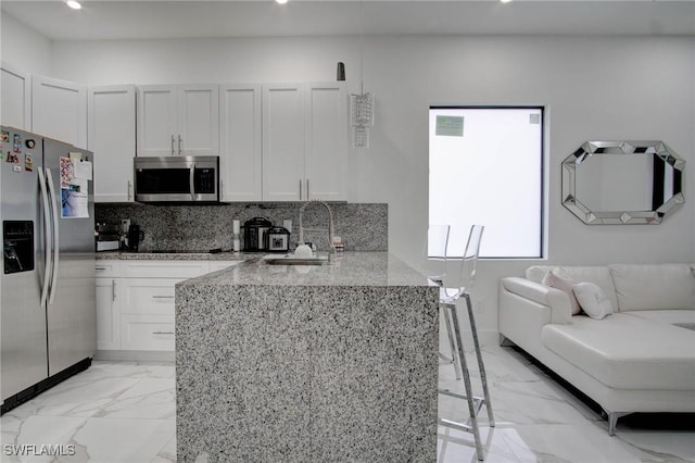 kitchen featuring a kitchen bar, appliances with stainless steel finishes, tasteful backsplash, sink, and white cabinets