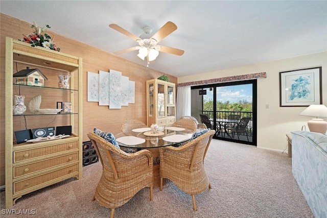 carpeted dining room featuring ceiling fan and wood walls