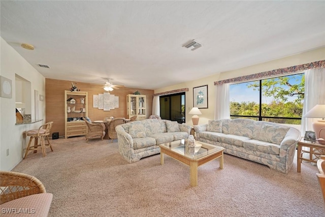 carpeted living room featuring ceiling fan and wood walls