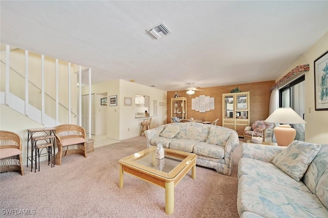 living room featuring ceiling fan, wooden walls, and light colored carpet