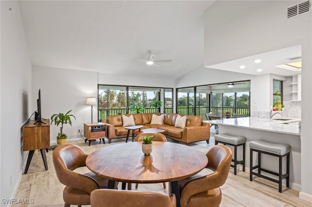 dining area with ceiling fan, sink, high vaulted ceiling, and light hardwood / wood-style floors