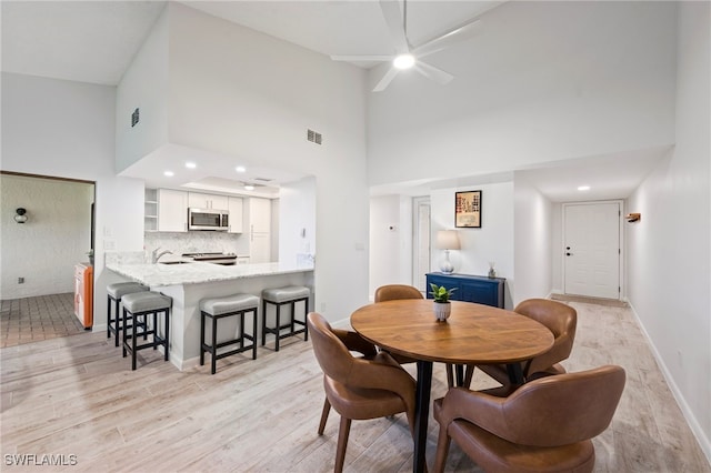 dining space featuring ceiling fan, sink, high vaulted ceiling, and light wood-type flooring