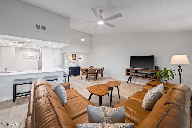 living room with ceiling fan, light wood-type flooring, sink, and high vaulted ceiling