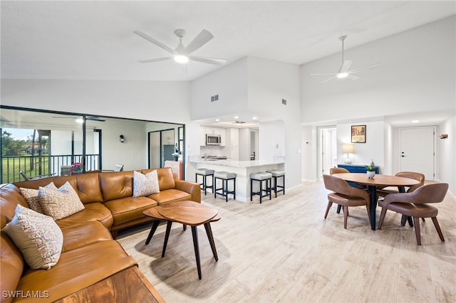 living room featuring ceiling fan, high vaulted ceiling, and light wood-type flooring