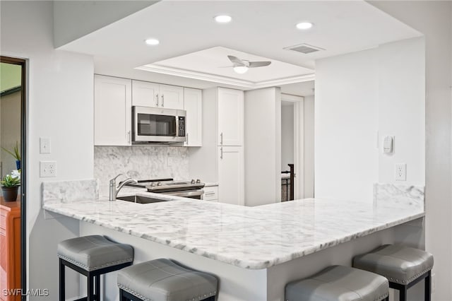 kitchen featuring backsplash, white cabinets, a kitchen bar, kitchen peninsula, and stainless steel appliances