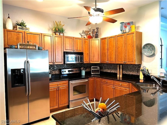 kitchen with appliances with stainless steel finishes, backsplash, ceiling fan, sink, and dark stone countertops