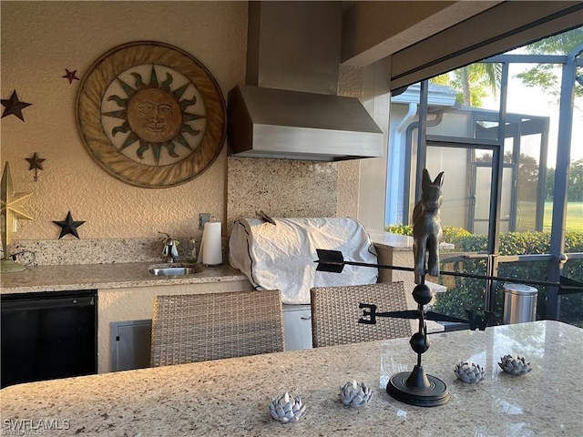 kitchen with dishwasher, sink, light stone counters, and wall chimney range hood