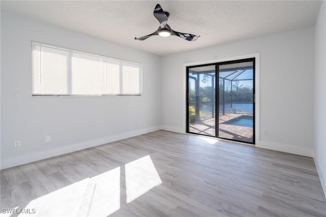 unfurnished room with a textured ceiling, ceiling fan, and light wood-type flooring