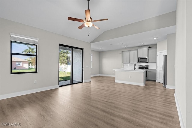 unfurnished living room featuring a sink, light wood-type flooring, a ceiling fan, lofted ceiling, and baseboards