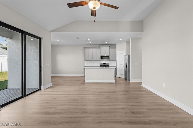 unfurnished living room with a ceiling fan, light wood-type flooring, vaulted ceiling, and baseboards
