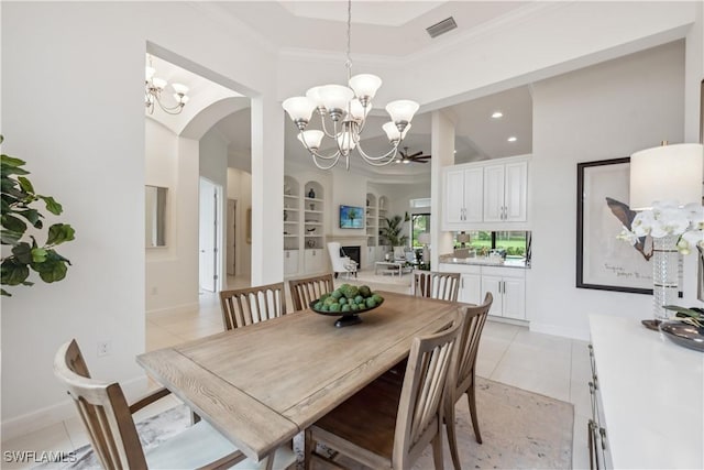 dining room featuring ceiling fan with notable chandelier, crown molding, built in shelves, light tile patterned floors, and a tray ceiling