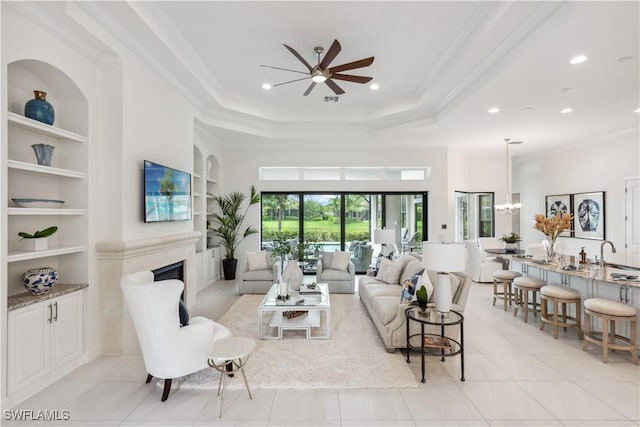 living room with built in shelves, light tile patterned floors, ceiling fan with notable chandelier, and ornamental molding