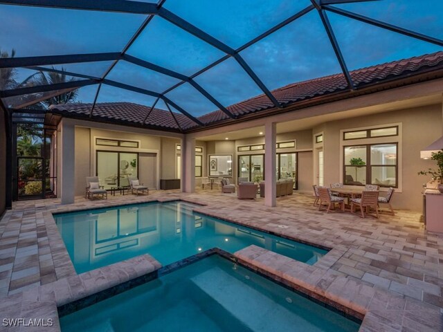 pool at dusk featuring glass enclosure, an in ground hot tub, a patio area, and an outdoor living space