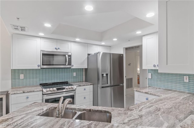 kitchen featuring sink, white cabinets, light stone counters, decorative backsplash, and appliances with stainless steel finishes