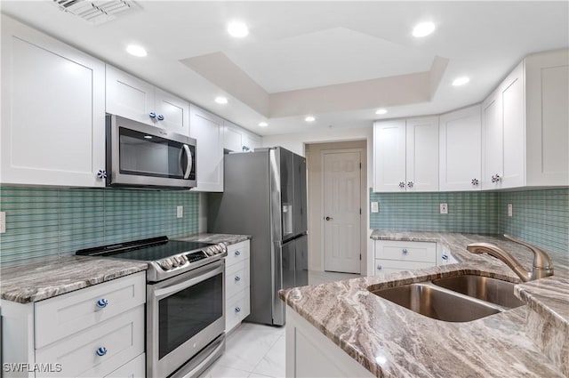 kitchen featuring stainless steel appliances, sink, white cabinets, light stone counters, and decorative backsplash