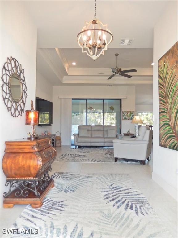 living room with ceiling fan with notable chandelier, a raised ceiling, and crown molding