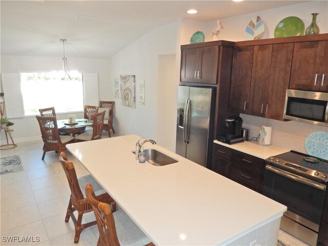 kitchen featuring sink, hanging light fixtures, stainless steel appliances, a notable chandelier, and an island with sink