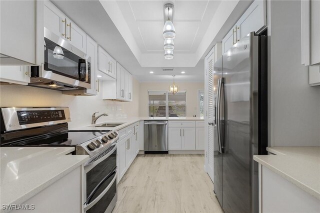 kitchen featuring sink, white cabinetry, hanging light fixtures, stainless steel appliances, and a tray ceiling