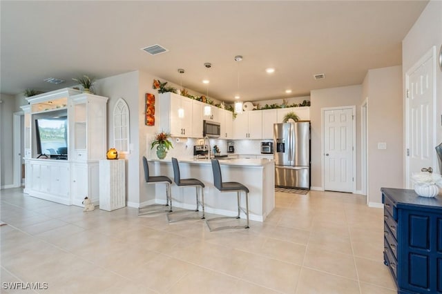 kitchen featuring white cabinets, decorative backsplash, light tile patterned floors, appliances with stainless steel finishes, and a breakfast bar area