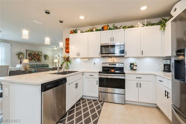 kitchen featuring kitchen peninsula, appliances with stainless steel finishes, sink, white cabinetry, and hanging light fixtures