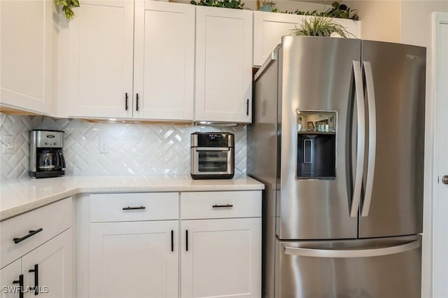 kitchen with white cabinets, stainless steel fridge, light stone counters, and backsplash